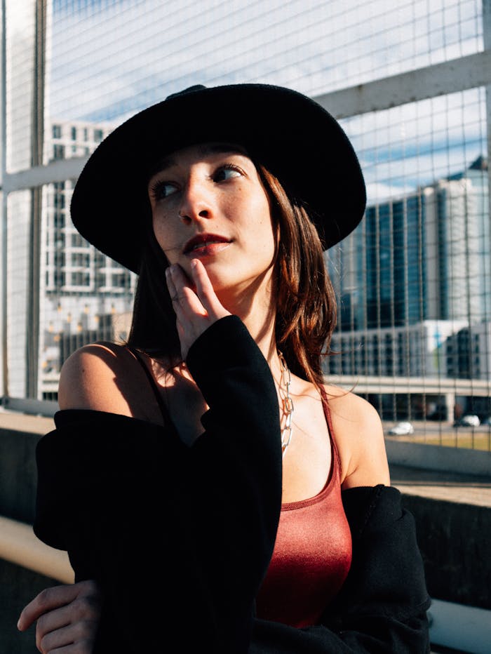 Fashionable woman in a hat poses against the backdrop of Atlanta's urban skyline, bathed in natural sunlight.